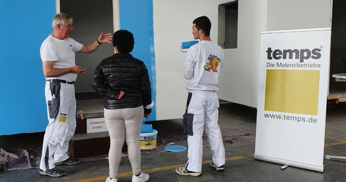 Ausbildungsleiter Andreas Hunsicker erklärt einer Interessentin beim Click & Meet bei temps , wie man eine Farbrolle hält